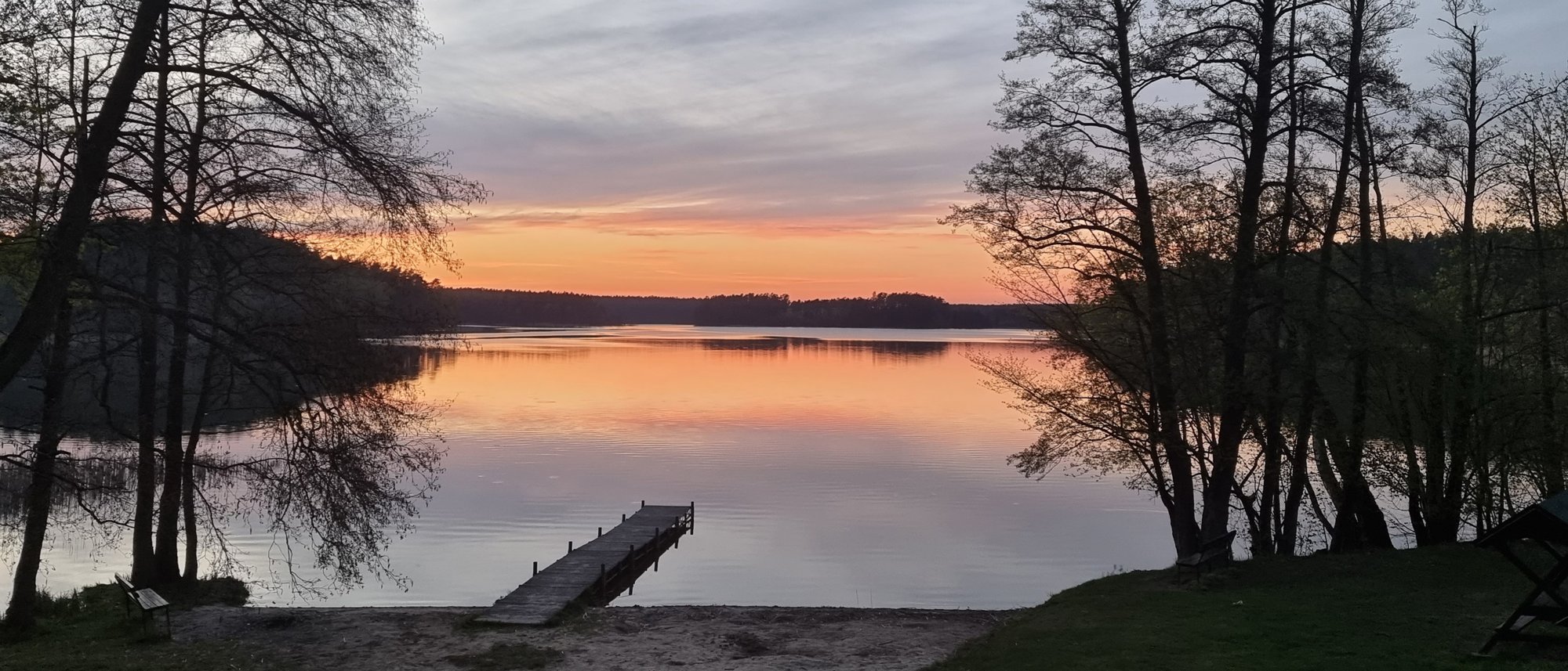 Zachód słońca nad jeziorem Sosno, pomost i drzewa na brzegu