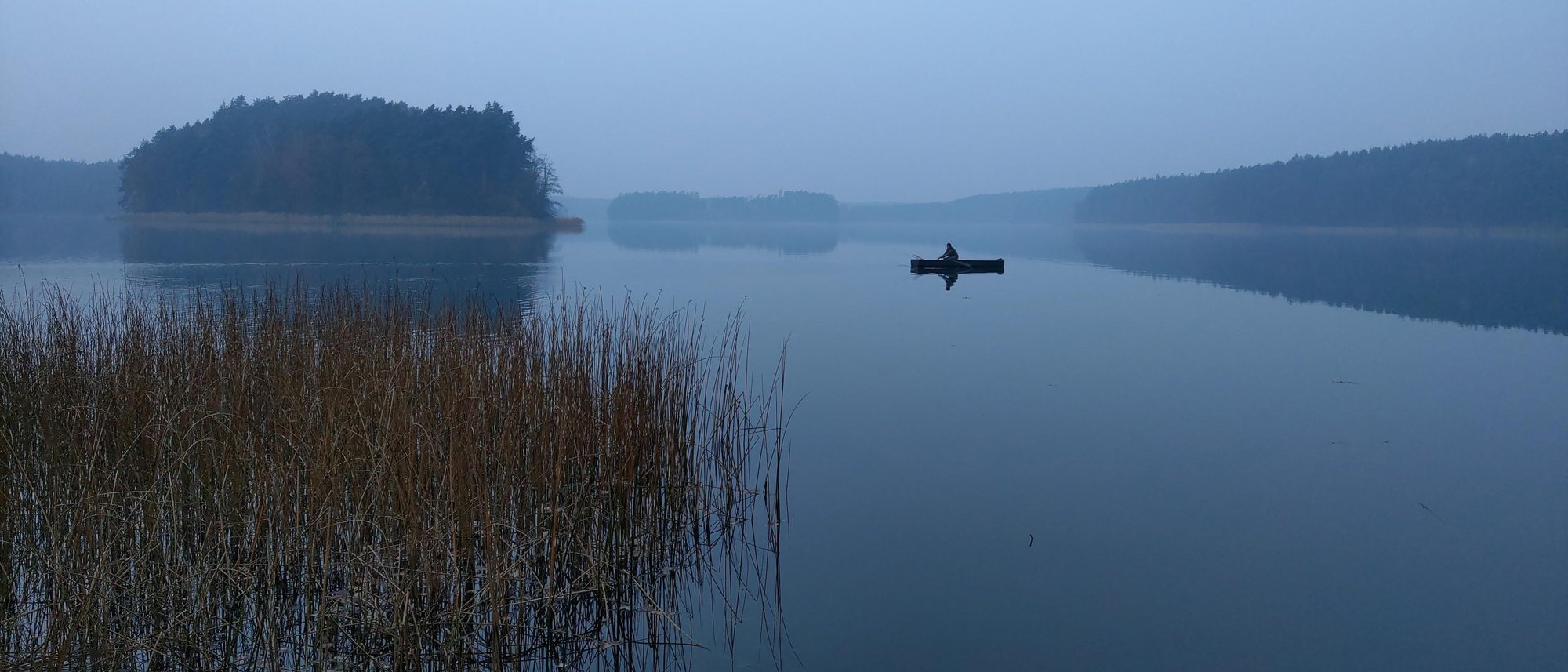 Wędkarz w łodzi na spokojnym jeziorze Sosno