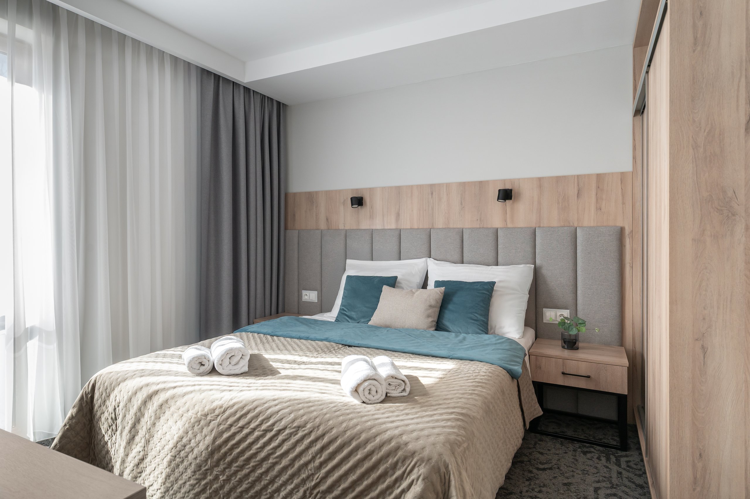Suite-Zimmer in der Residenz AMBRE in Łeba mit Schlafzimmer, Bett, türkisfarbenen Kissen und Handtüchern.