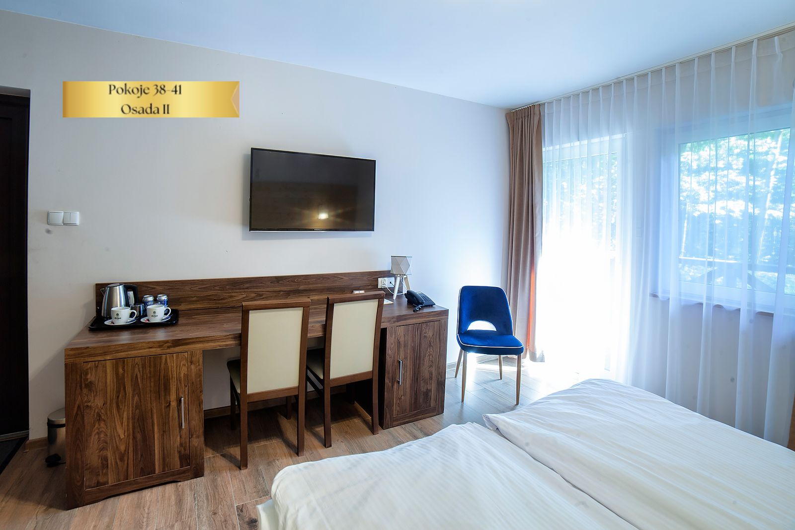 Pokój Comfort Plus w Osadzie II – biurko z krzesłami i okno na zieleń