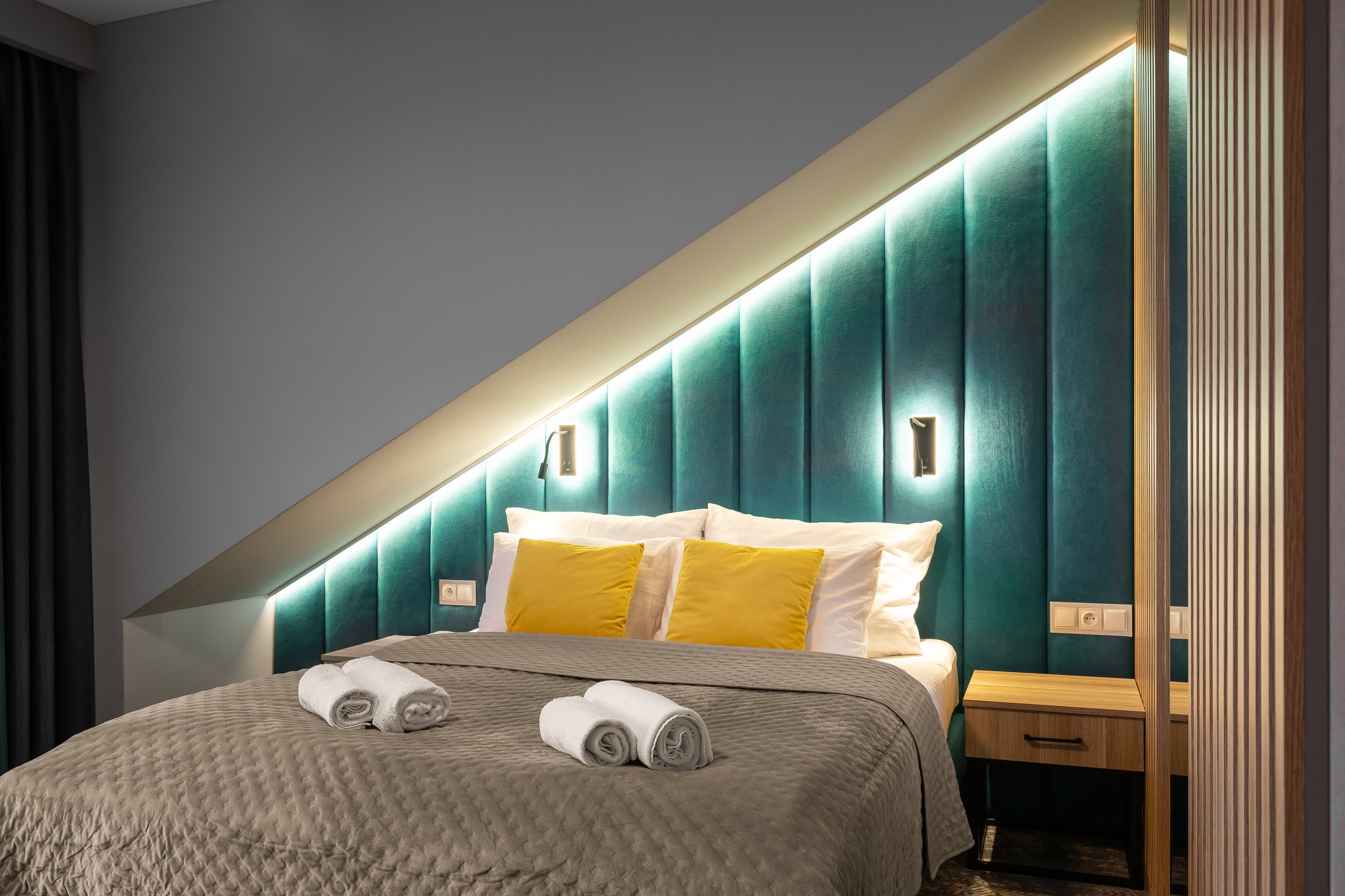 Superior-Zimmer in der Residenz AMBRE in Łeba mit Bett und türkisfarbenem, hintergrundbeleuchtetem Kopfteil unter einer Schräge.