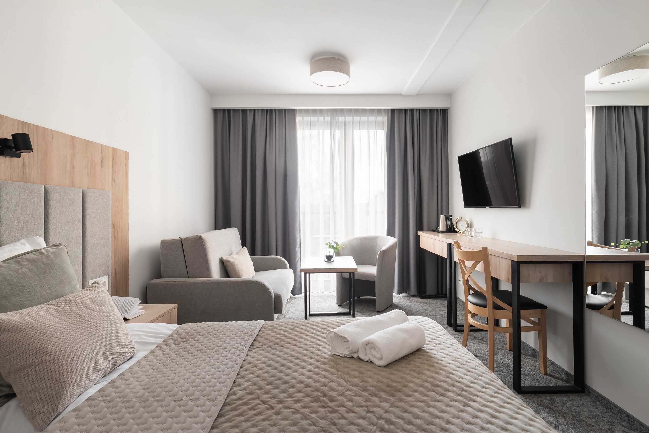 Superior-Junior-Zimmer in der Residenz AMBRE in Łeba mit Bett, Schlafsofa, Sessel und Schreibtisch mit Fernseher.