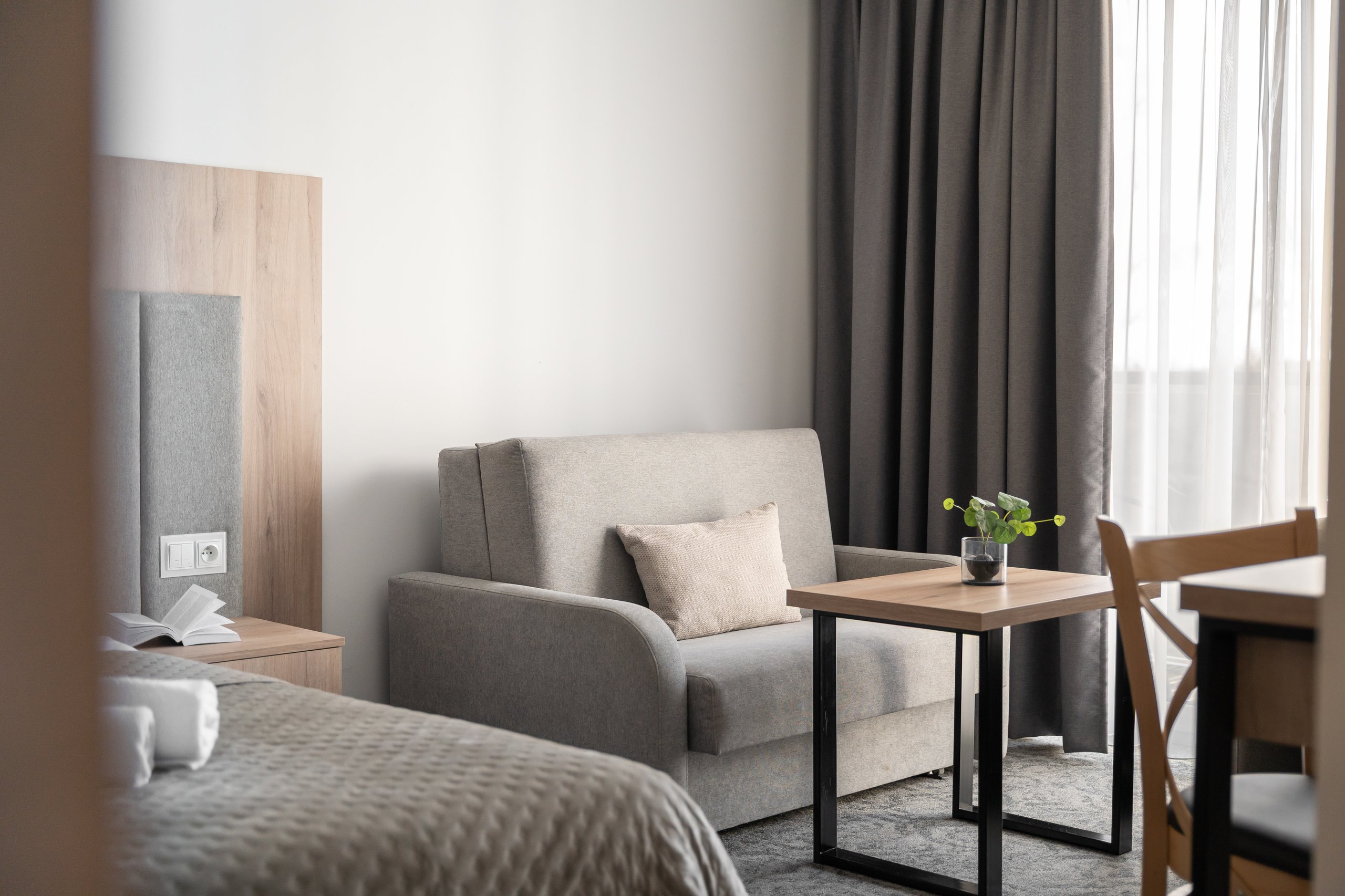 Superior-Junior-Zimmer in der Residenz AMBRE in Łeba mit Schlafsofa und Tisch mit Pflanze am Fenster.