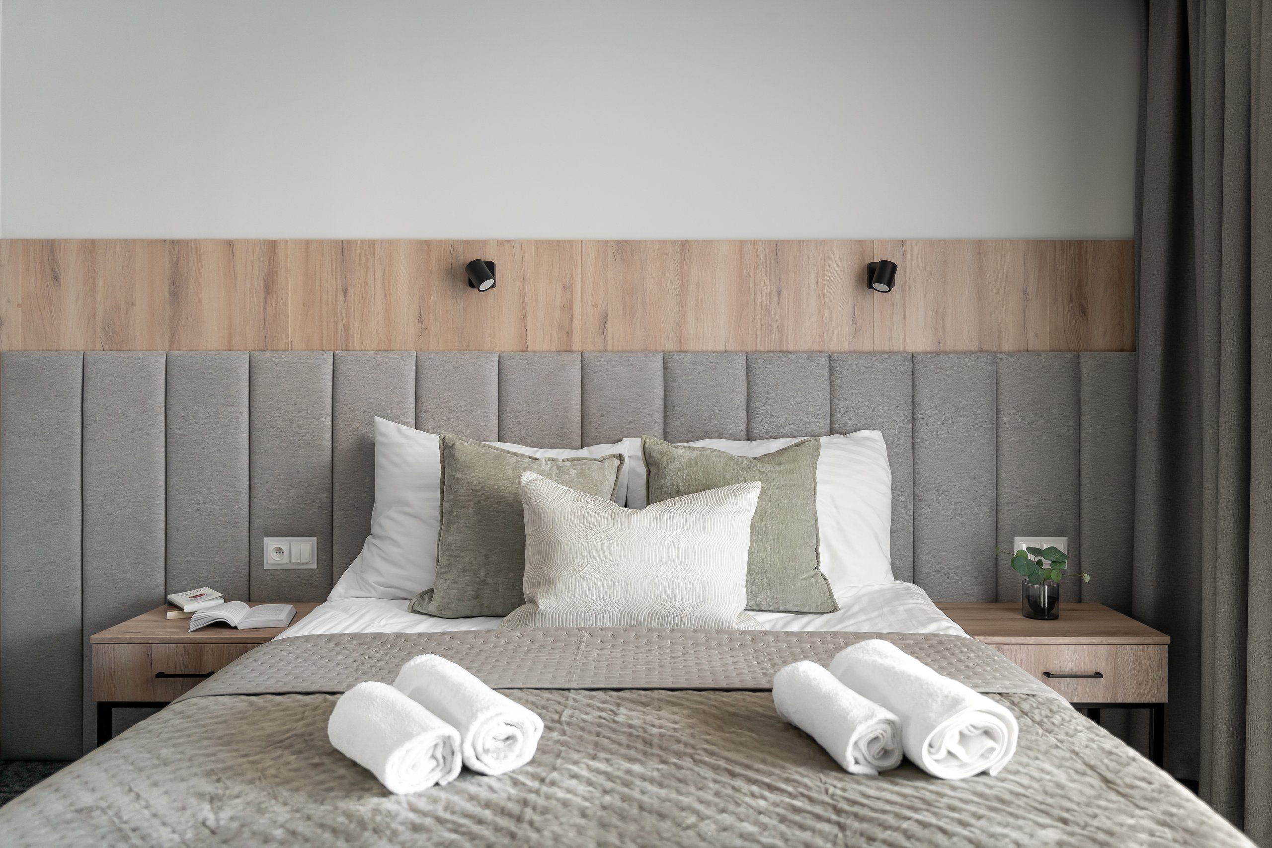 Comfort-Plus-Zimmer in der Residenz AMBRE in Łeba mit Bett, grauem gepolstertem Kopfteil und aufgerollten Handtüchern.