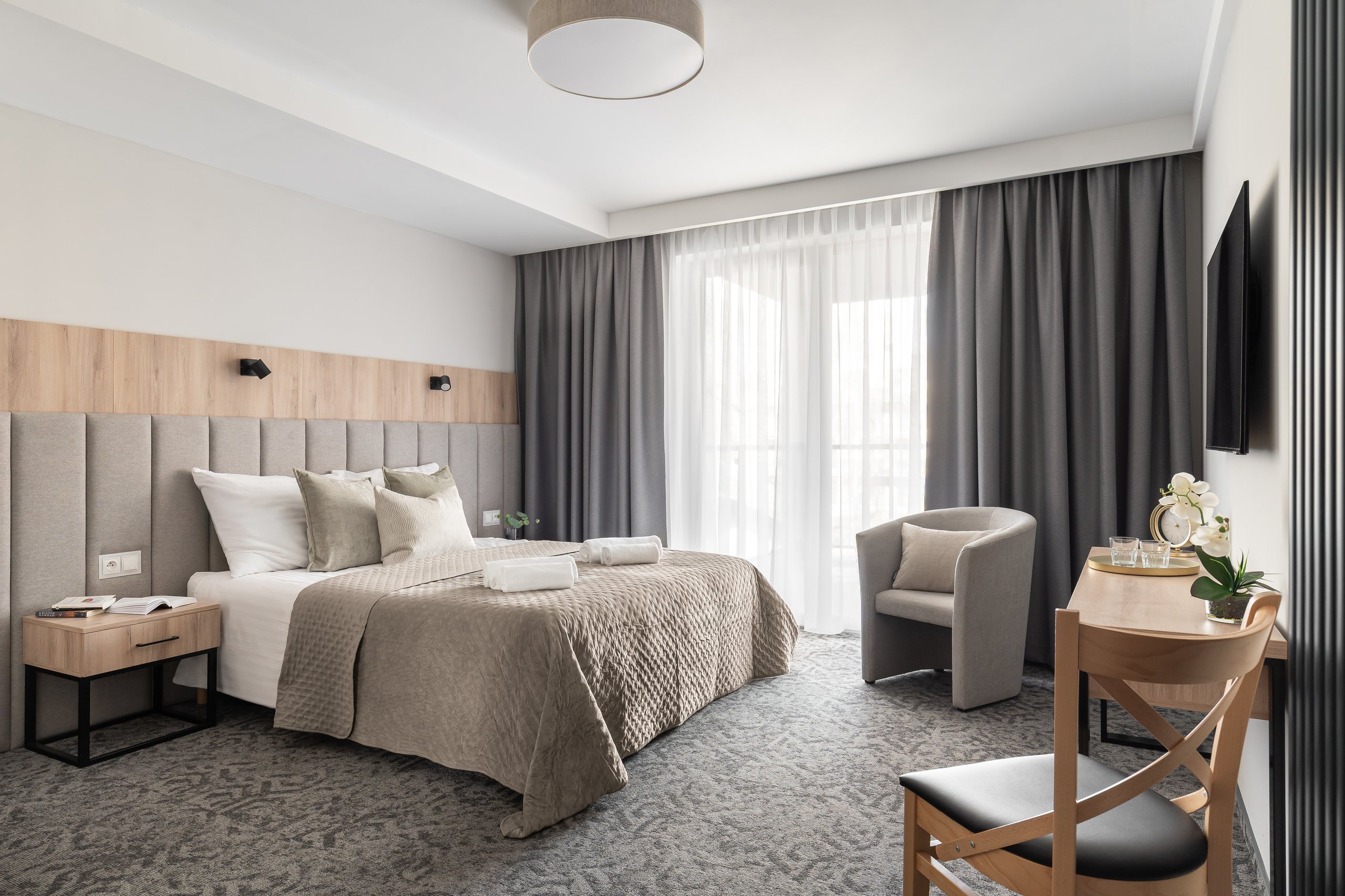 Comfort-Plus-Zimmer in der Residenz AMBRE in Łeba – Bett mit gepolstertem Kopfteil, Sessel und Schreibtisch am Fenster.