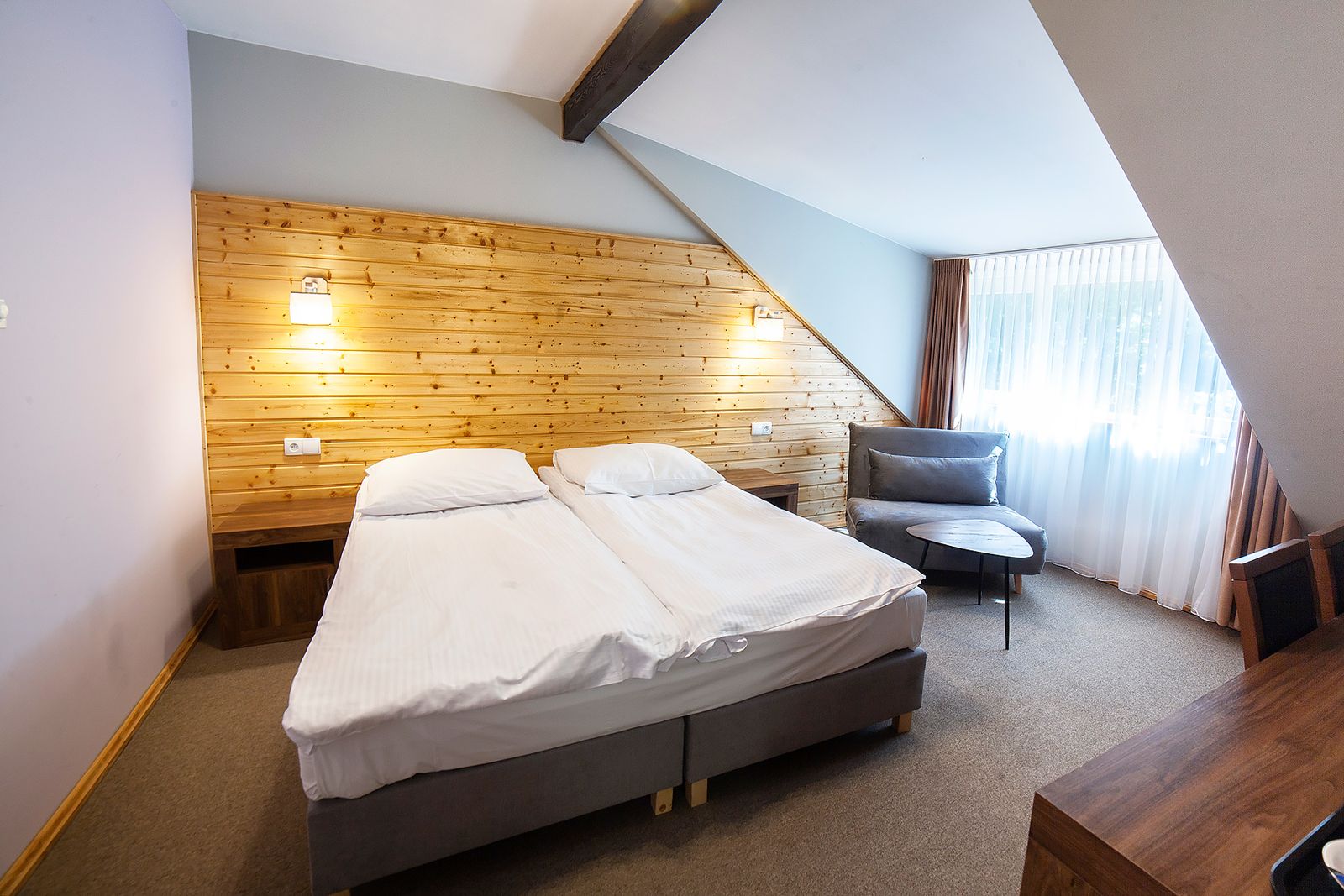 Pokój Comfort w Dworku Wapionka – łóżko, drewniana ściana i fotel przy oknie