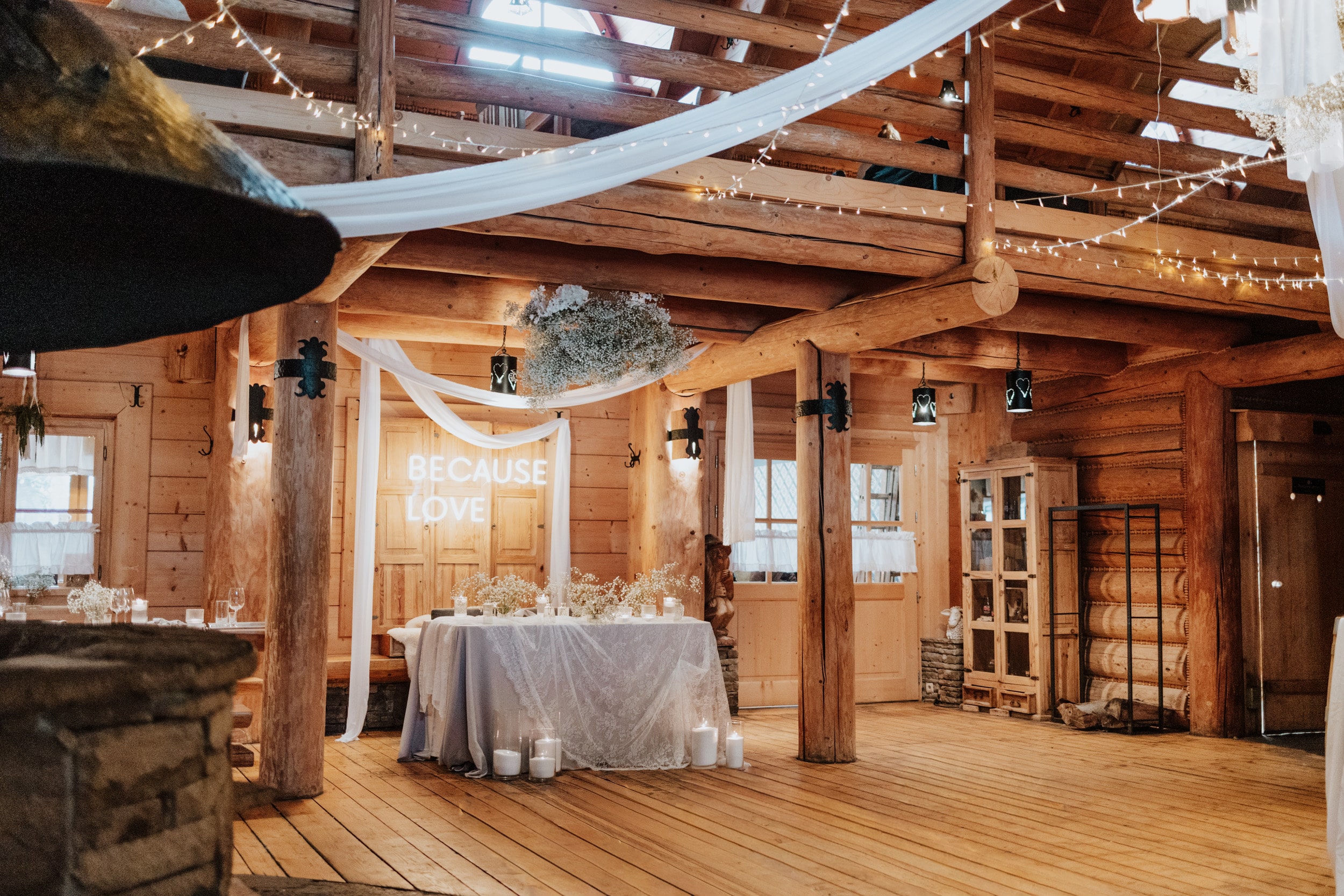 Decorated wooden hall with draped fabric, baby's-breath florals and neon Because Love sign, intimate.