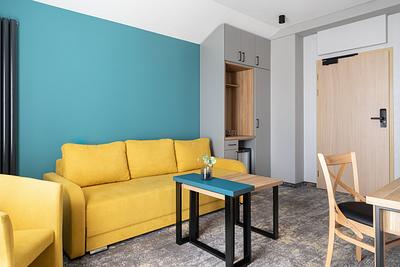 Premium-Suite-Zimmer in der Residenz AMBRE in Łeba mit gelber Schlafcouch, einem Kaffeetisch und einer türkisfarbenen Wand.