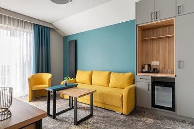 Premium-Suite-Zimmer in der Residenz AMBRE in Łeba mit gelber Couch und Sessel an einer türkisfarbenen Wand sowie einer Kochnische mit Wasserkocher.
