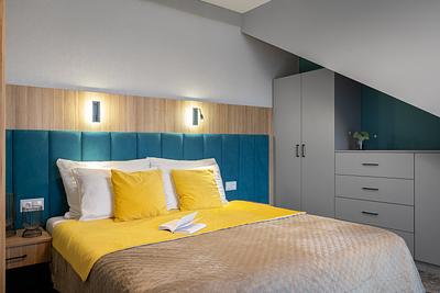 Premium-Suite-Zimmer in der Residenz AMBRE in Łeba mit Schlafzimmer, türkisfarbenem Kopfteil und gelben Kissen.
