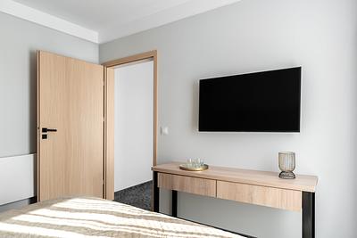Suite-Zimmer in der Residenz AMBRE in Łeba mit an der Wand montiertem Fernseher und einem Schreibtisch neben einer offenen Tür.
