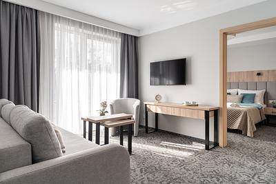 Suite-Zimmer in der Residenz AMBRE in Łeba mit Wohnbereich, grauer Couch, Sessel und Schreibtisch, daneben ein separates Schlafzimmer.
