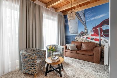 Apartment Maisonette Comfort Plus in der Residenz AMBRE in Łeba – Wohnzimmer mit Fototapete mit Segelbootmotiv, Ledersofa und Sesseln.
