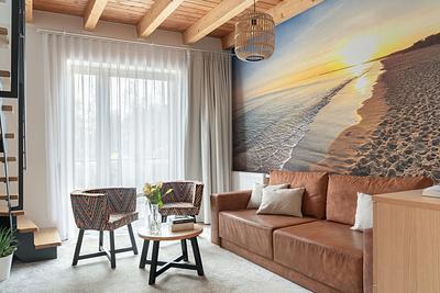 Apartment Maisonette Comfort in der Residenz AMBRE in Łeba – Wohnzimmer mit Fototapete mit Strandmotiv, Ledersofa und Sesseln.