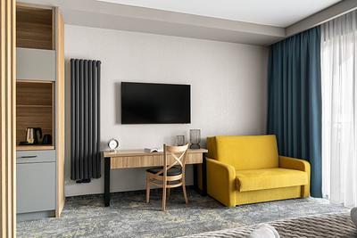 Superior-Zimmer in der Residenz AMBRE in Łeba mit gelbem Schlafsofa, Schreibtisch und Fernseher am Fenster.