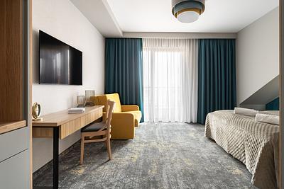 Superior-Zimmer in der Residenz AMBRE in Łeba mit Schreibtisch, gelbem Sessel und Fenster mit maritimen Vorhängen.