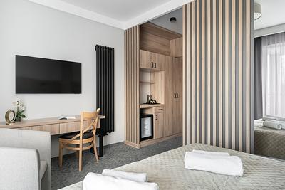 Comfort-Zimmer in der Residenz AMBRE in Łeba – Schreibtisch mit Stuhl, Fernseher an der Wand und Schrank mit Kühlschrank.