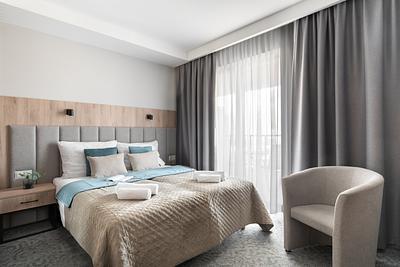 Comfort-Zimmer in der Residenz AMBRE in Łeba – Bett mit türkisfarbenen Akzenten und Sessel am Fenster.