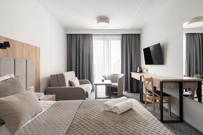 Superior-Junior-Zimmer in der Residenz AMBRE in Łeba mit Bett, Schlafsofa, Sessel und Schreibtisch mit Fernseher.