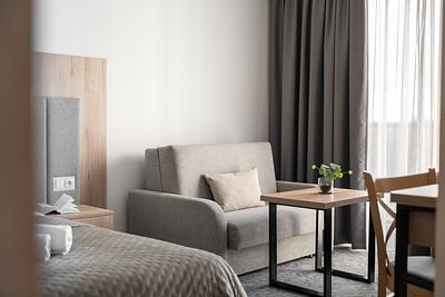 Superior-Junior-Zimmer in der Residenz AMBRE in Łeba mit Schlafsofa und Tisch mit Pflanze am Fenster.