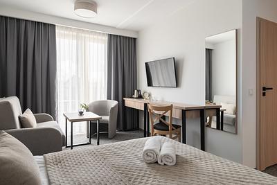 Superior-Junior-Zimmer in der Residenz AMBRE in Łeba mit Bett, zwei Sesseln am Fenster, Schreibtisch und Fernseher.