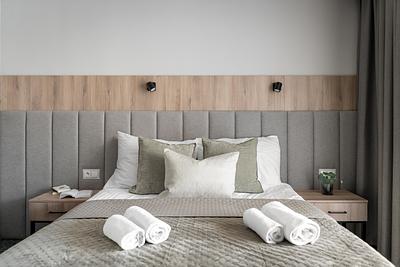 Comfort-Plus-Zimmer in der Residenz AMBRE in Łeba mit Bett, grauem gepolstertem Kopfteil und aufgerollten Handtüchern.