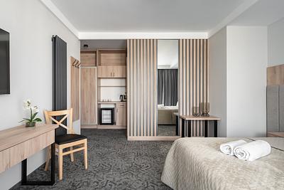 Comfort-Plus-Zimmer in der Residenz AMBRE in Łeba – Schreibtisch, Schrank mit Regalen und Kühlschrank sowie Lamellenwand.