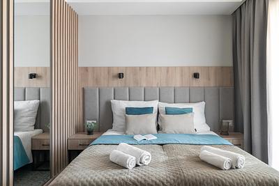 Comfort-Zimmer in der Residenz AMBRE in Łeba – Bett mit gepolstertem Kopfteil, türkisfarbenem Plaid und Handtüchern.